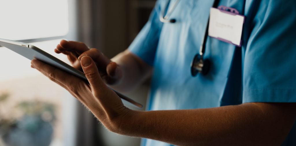 Female doctor in scrubs with digital tablet, typing and completing checklist.